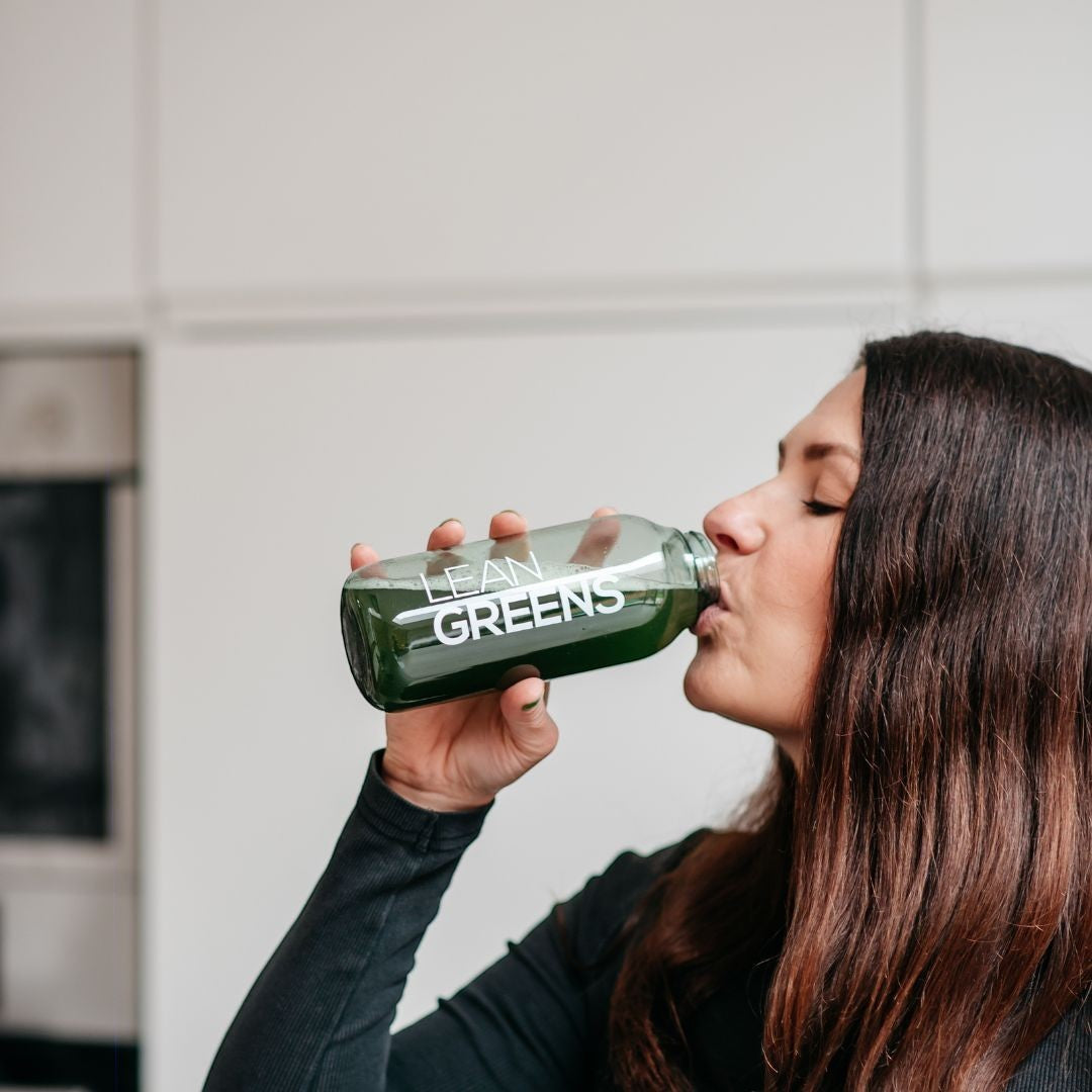 Woman drinking Lean Greens super greens powder from a bottle. Green nutritional supplement.