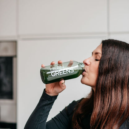 Woman drinking Lean Greens super greens powder from a bottle. Green nutritional supplement.