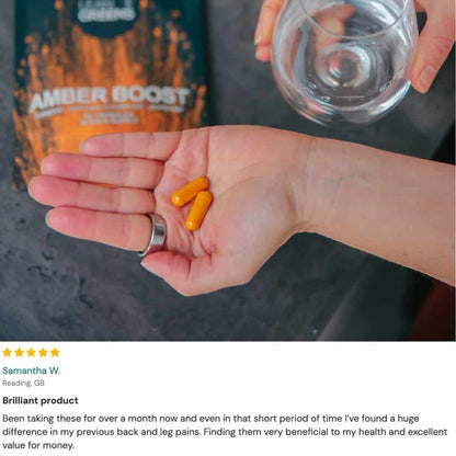W/end Amber Boost turmeric and curcumin capsules in orange, held in a hand with a glass of water.