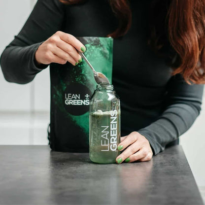 W/end Lean Greens super greens powder being added to a bottle of water with a spoon. Green powder and bottle.
